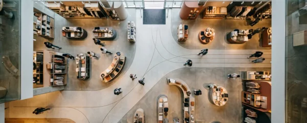 Vue aérienne d'un espace de vente moderne avec des clients suivant un parcours visuel naturel guidé par l'éclairage directionnel et le design d'espace